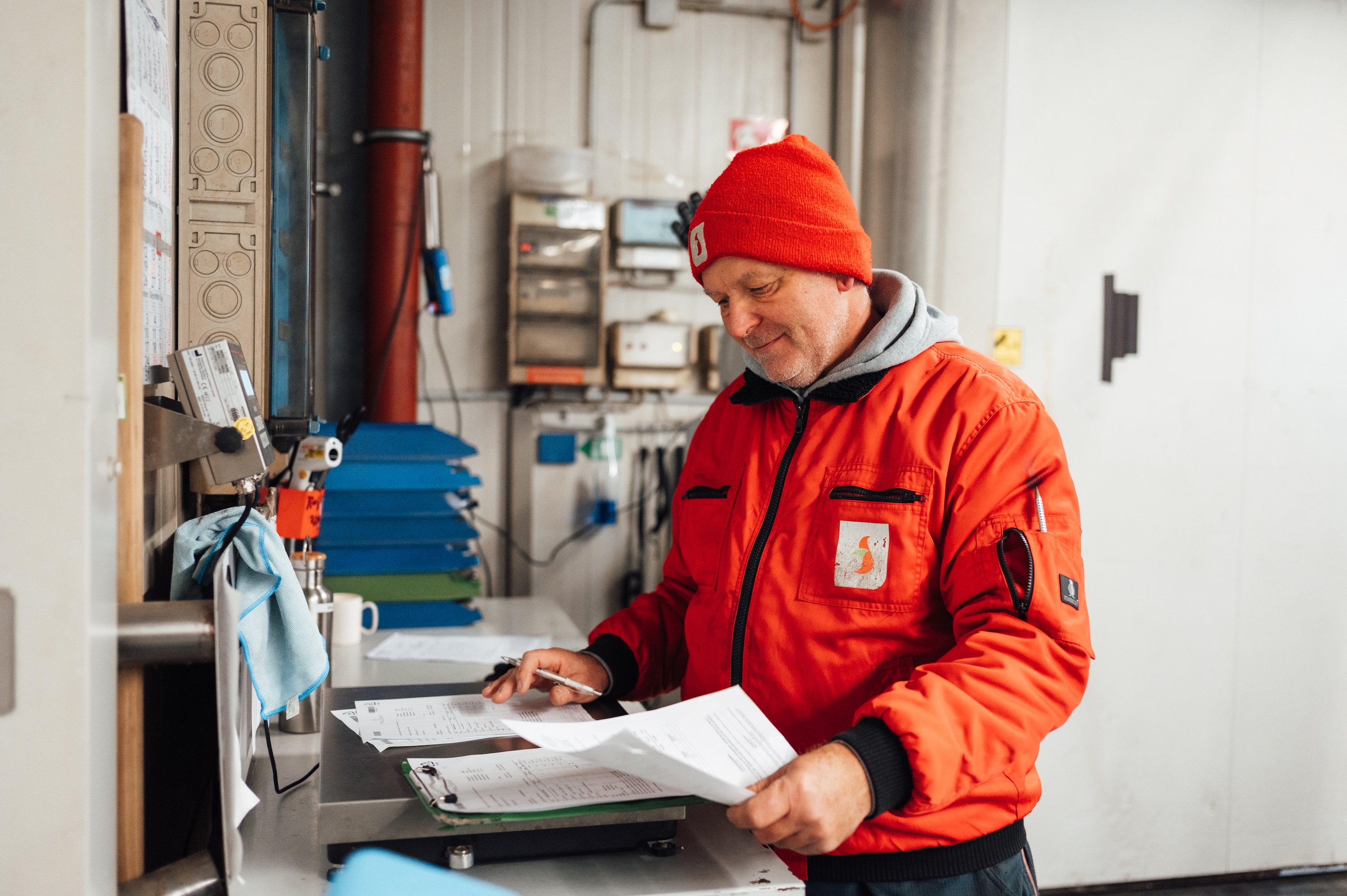 Ein Mann in roter Mütze und orangefarbener Jacke hält Papiere.