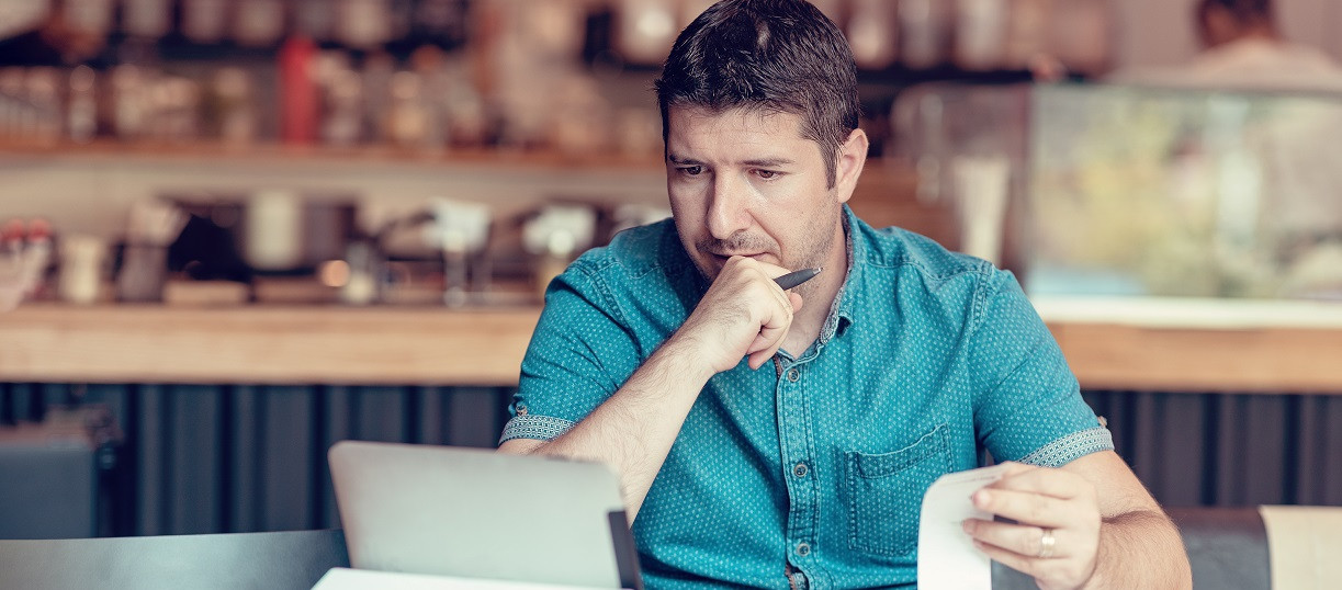 Angst als Geschäftsmodell Ein Mann sitzt an einem Tisch mit einem Laptop und einer Quittung.