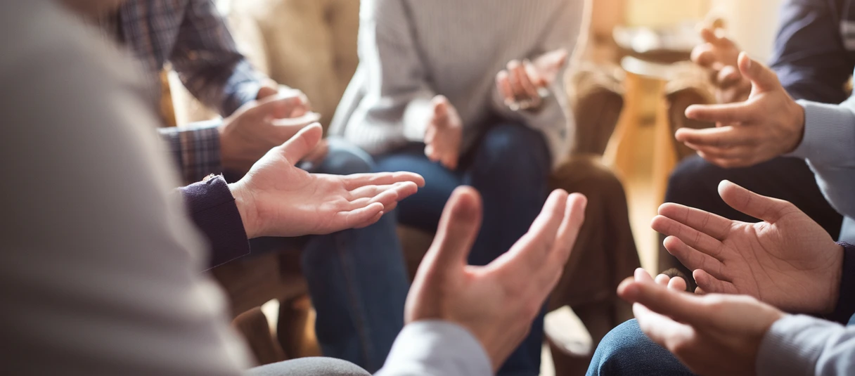 Faule Kompromisse Eine Gruppe von Menschen sitzt im Kreis und gestikuliert mit den Händen.