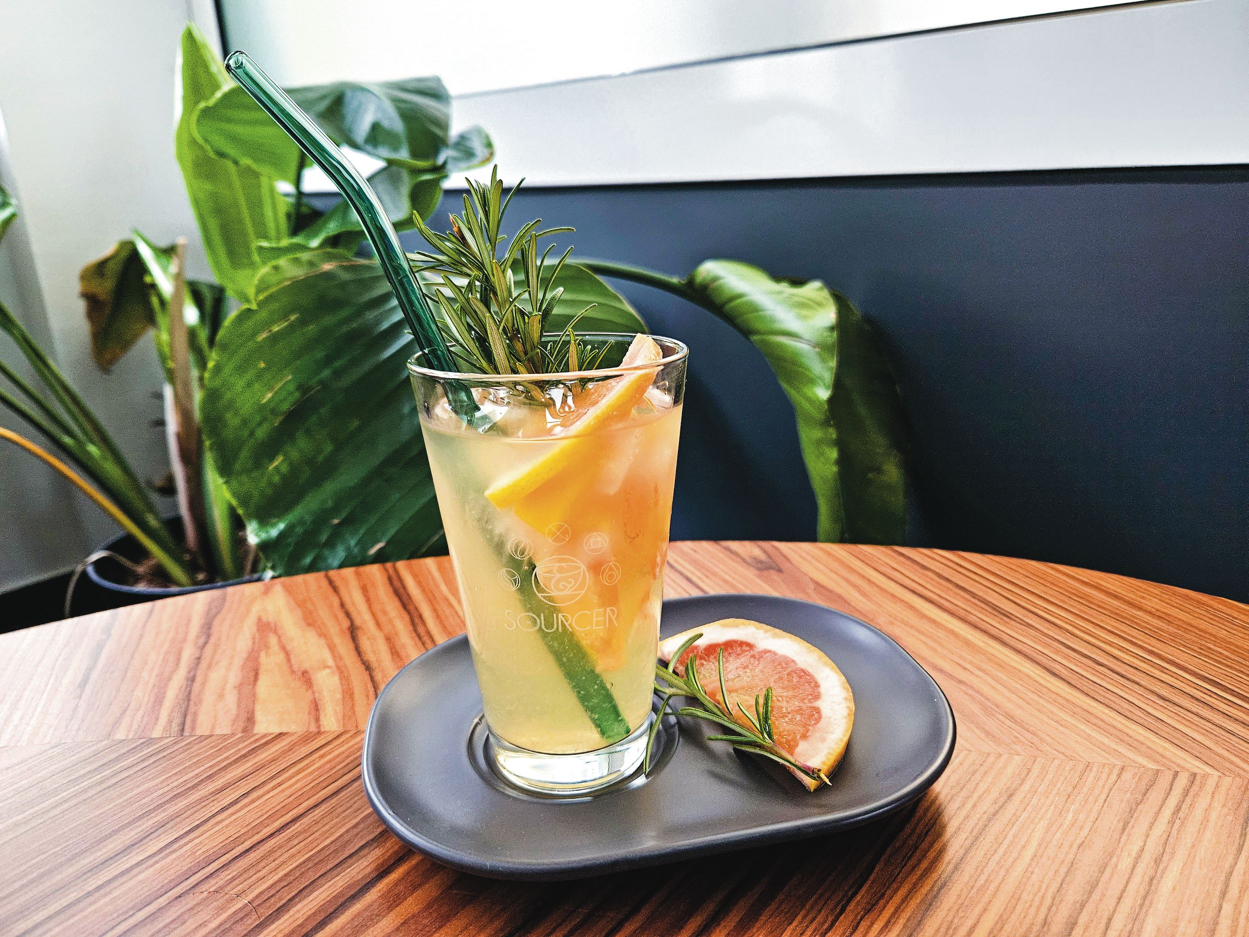 Ein Glas Getränk mit einem Strohhalm und einer Orangenscheibe auf einem Teller.