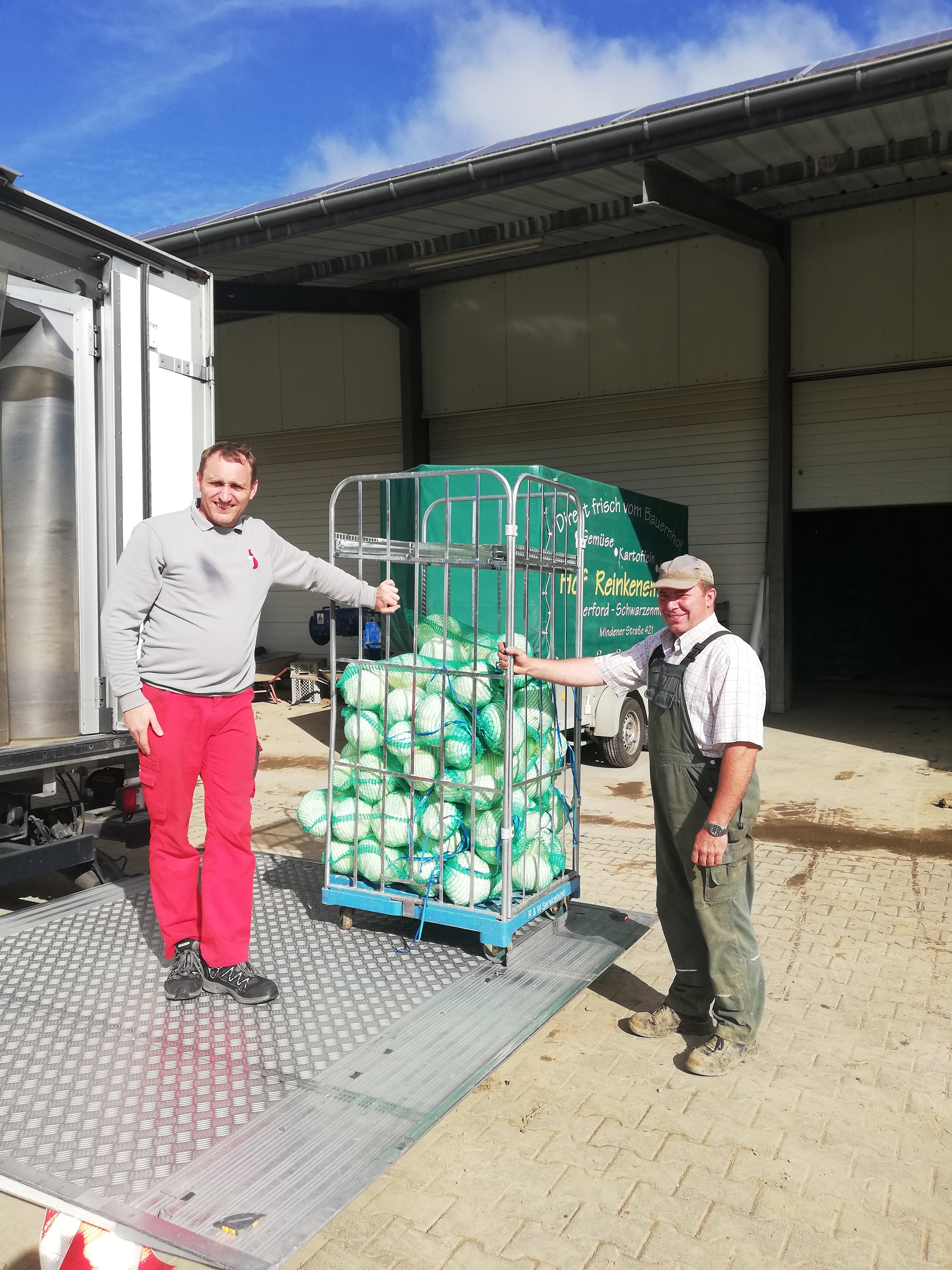 Zwei Männer stehen neben einem großen Metallkäfig mit grünen Objekten darin.