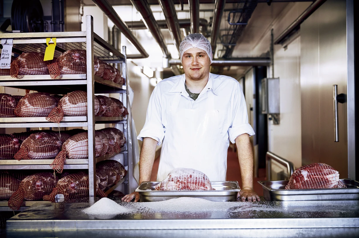 Ein Mann im weißen Kittel steht in einem Raum mit Fleisch.