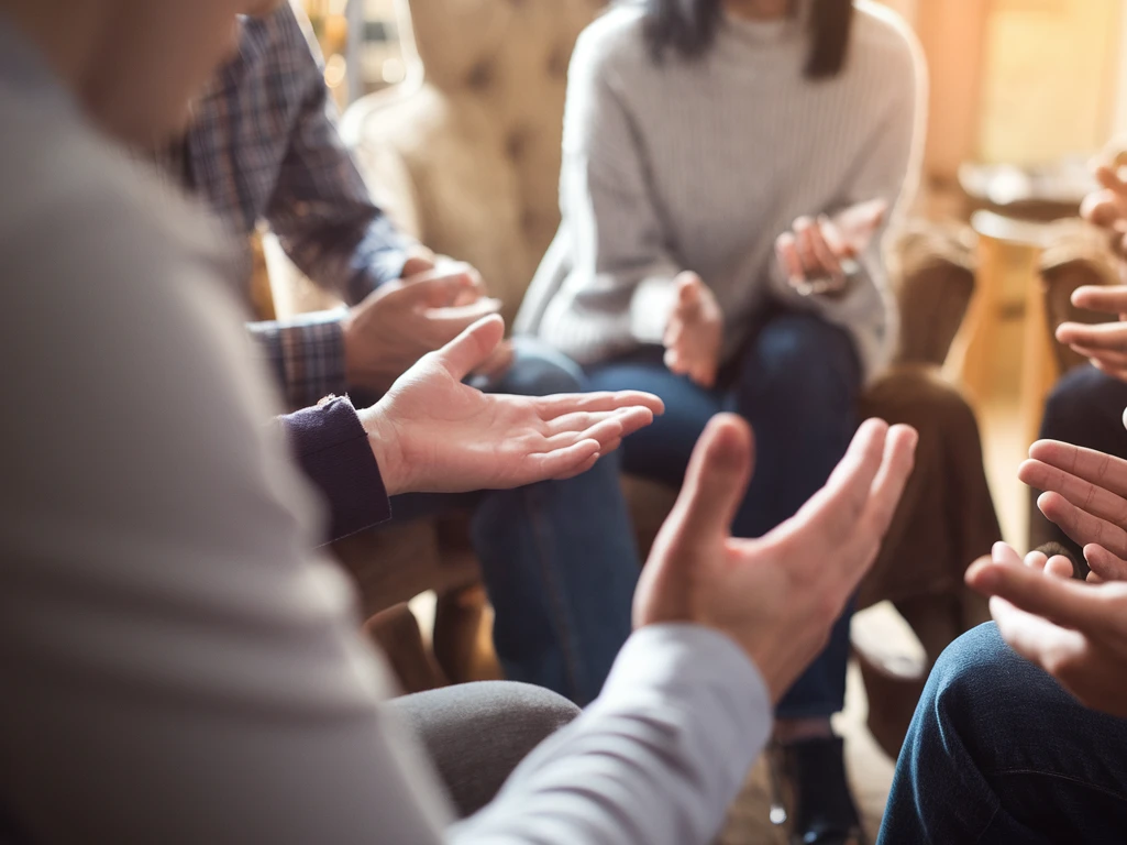 Eine Gruppe von Menschen sitzt im Kreis und gestikuliert mit den Händen.